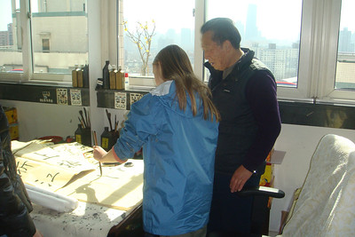 Alayna trying her hand at caligraphy as Mr. Mai looks on
